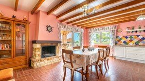 Un coin repas agrémenté d’une cheminée, de poutres en bois, d’un lustre et d’un revêtement mural aux couleurs vives.