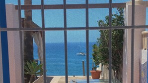 Un patio iluminado por el sol con vistas al mar, una mesa, sillas y plantas en macetas.