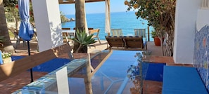 A patio with a glass table, wooden chairs, and a view of the sea.