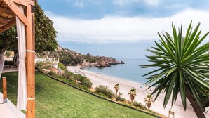 Vista costera con una playa, una pérgola de madera y una planta de agave grande.