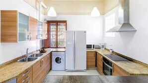 Una cocina moderna con refrigerador de acero inoxidable, lavadora, armarios de madera e iluminación colgante.