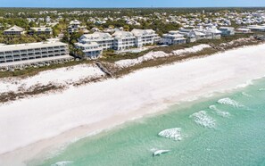 An aerial view of a coastal area with beachfront properties, a sandy beach, and clear turquoise waters.