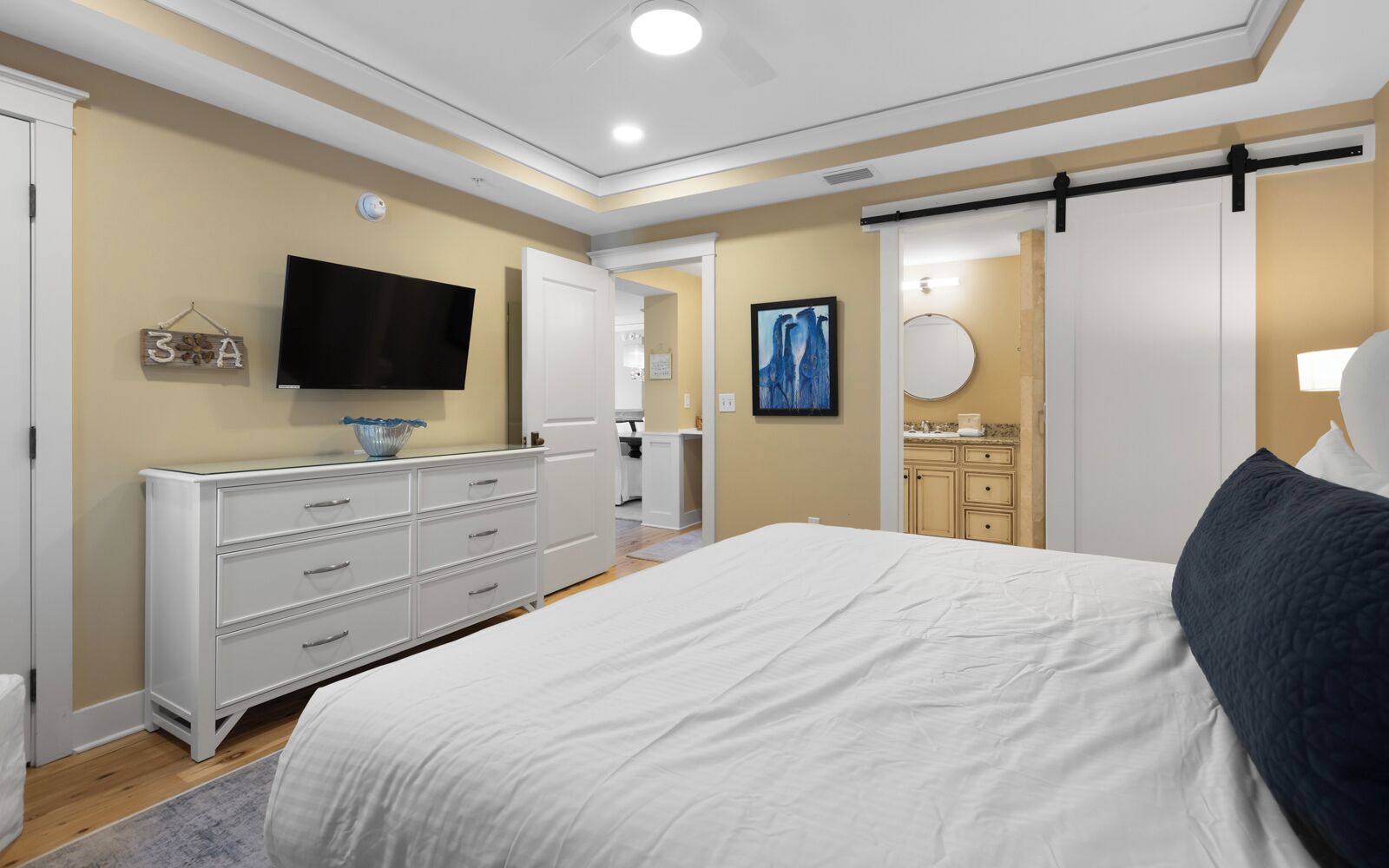 A bedroom with a bed, dresser, TV, and a bathroom with a sink and mirror.
