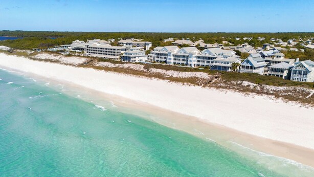 Luchtbeeld van een kusthotel met kamers aan het strand, een zandstrand en een heldere blauwe zee.