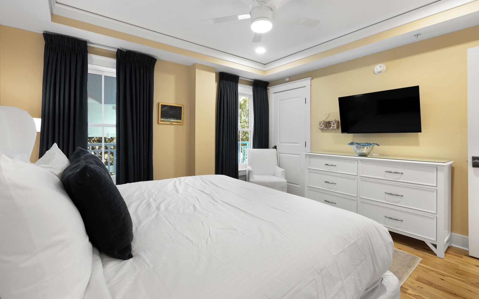 Una camera d'albergo con un letto grande, una TV a muro, un comò e una finestra con tende.
