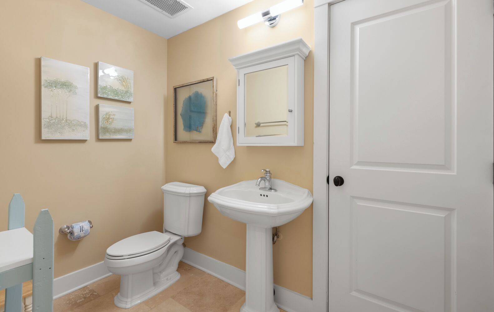 A bathroom with a toilet, sink, and a door. There are wall-mounted artworks and a towel hanging on the wall.