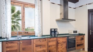 A kitchen with wooden cabinets, a built-in oven, a microwave, and a window with curtains.