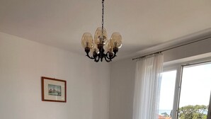 Un dormitorio con cama de madera, candelabro, mesita de noche, un cuadro enmarco y vistas al exterior.