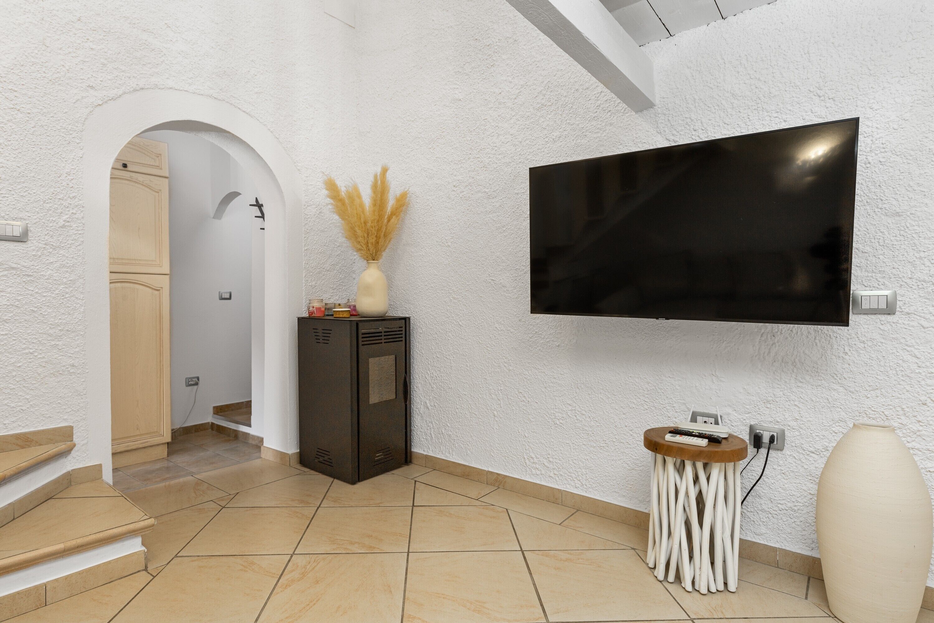 A modern interior with a flat-screen TV mounted on the wall, a small wooden side table with a vase, and a staircase leading to another room.