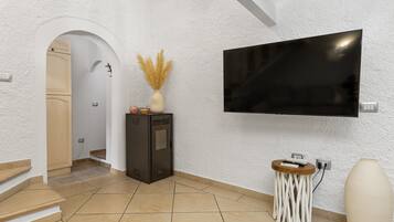 A modern interior with a flat-screen TV mounted on the wall, a small wooden side table with a vase, and a staircase leading to another room.