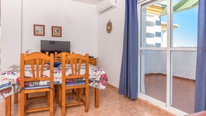 Ein Zimmer mit Esstisch, Stühlen, Fernseher und einer Schiebetür zu einem Außenbereich.