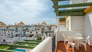 Eine Terrasse mit Pool, weißen Möbeln und Blick auf ein Wohngebiet mit weißen Gebäuden.