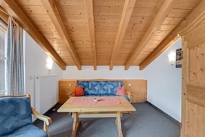 Une pièce avec un plafond en bois, un lit recouvert d’une literie à motifs, une table et une chaise.