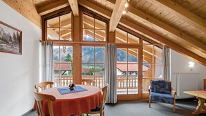 A room with a wooden ceiling, large windows, a dining table with chairs, and a sofa. - Charming Apartment “Petrushof Rechenberg” with Mountain View, Wi-Fi, Balcony (Oberwössen)