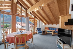 A wooden interior with a dining table, chairs, a sofa, and a TV. - Charming Apartment “Petrushof Rechenberg” with Mountain View, Wi-Fi, Balcony (Oberwössen)