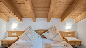 A room with wooden beams, a bed with floral pillows, bedside tables, and wall-mounted lights. - Charming Apartment “Petrushof Rechenberg” with Mountain View, Wi-Fi, Balcony (Oberwössen)