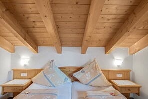 A room with wooden beams, a bed with floral pillows, bedside tables, and wall-mounted lights.