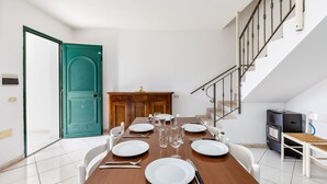 A dining area with a table set for four, a teal door, a staircase, and a small heater. - Charming Holiday Home Tanaunella appartamento 2 with Ventilators, Balcony, Terraces & Sea View; Parking Available, Pets Allowed (tanaunella)