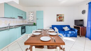 A compact living space with a kitchen, dining area, and a blue sofa. - Charming Holiday Home Tanaunella appartamento 2 with Ventilators, Balcony, Terraces & Sea View; Parking Available, Pets Allowed (tanaunella)