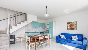 A modern kitchen with teal cabinets, a dining area with a wooden table and chairs, a blue sofa, and a staircase. - Charming Holiday Home Tanaunella appartamento 2 with Ventilators, Balcony, Terraces & Sea View; Parking Available, Pets Allowed (tanaunella)