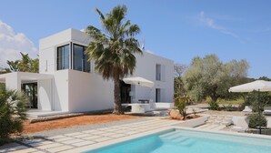 Une maison moderne à deux étages, dotée d’une piscine, d’un espace salon extérieur et de palmiers.
