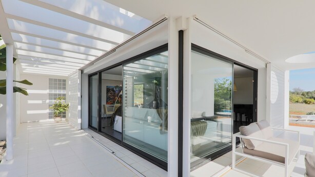 Un espace de vie extérieur moderne, doté de murs en verre, d’une terrasse blanche et offrant une vue sur le paysage.
