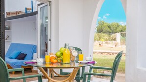 Ein Glastisch mit Frühstücksangeboten, ein blaues Sofa und Blick auf Grünflächen.
