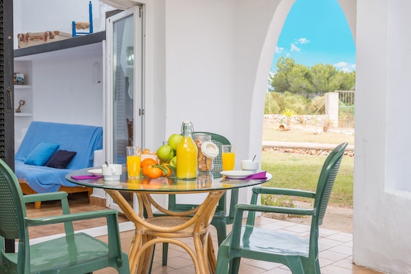 A glass table with breakfast items, a blue sofa, and a view of greenery.