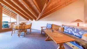 A room with a wooden ceiling, a sofa, a table, and chairs.