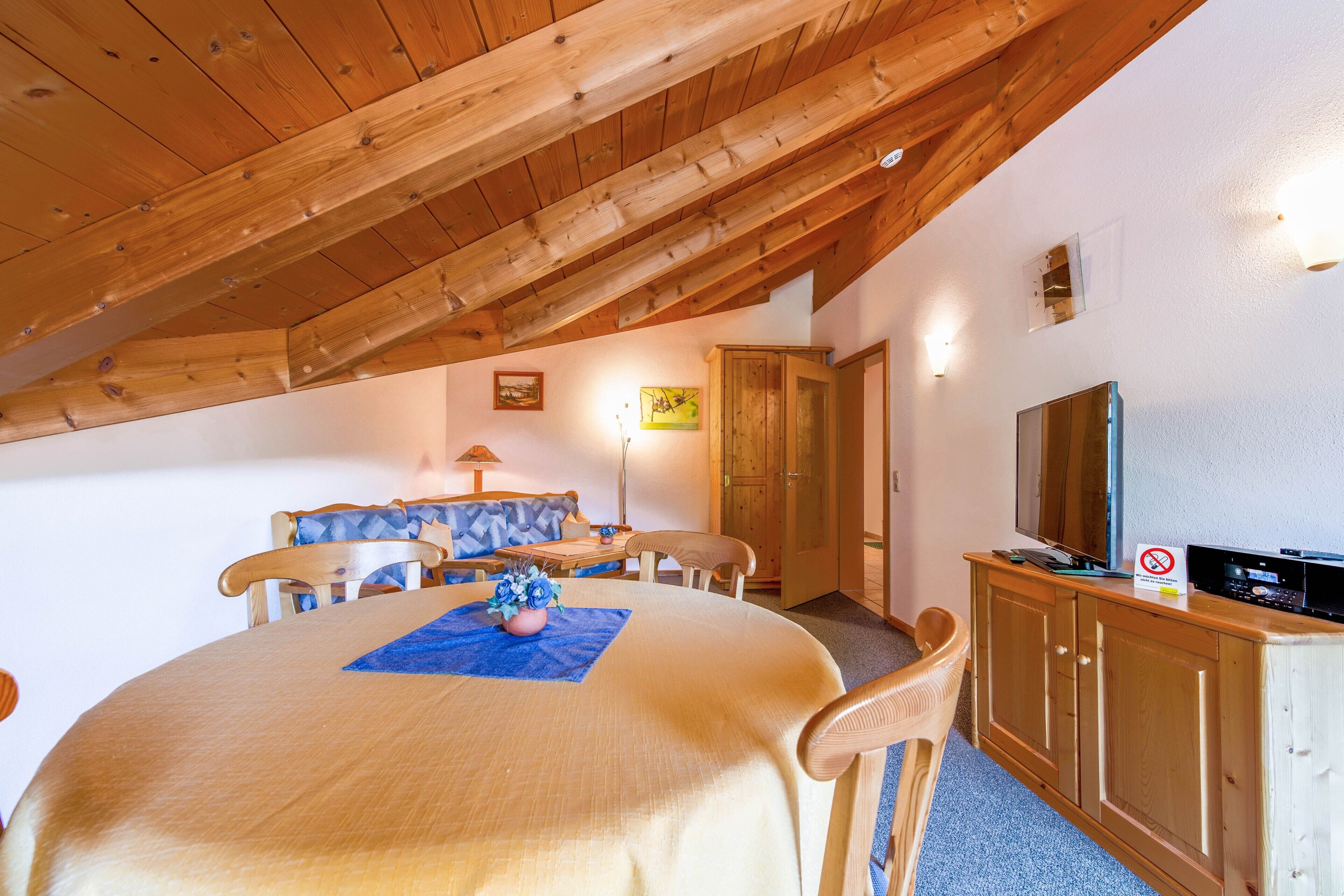 Ein Essbereich mit Holzboden, einem Tisch mit blauer Tischdecke und einem Fernseher auf einer Holzkommode.