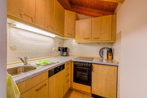 A compact kitchen with wooden cabinets, a dishwasher, an oven, and a countertop with a coffee maker.