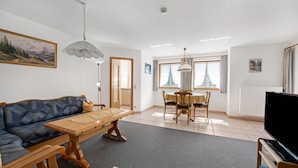 A living room with a sofa, a wooden table, a TV, and a dining area with chairs and a table. - Apartment “Petrushof Ferienwohnung Taubensee” with Mountain View, Wi-Fi, Balcony (Oberwössen)
