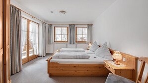 A bedroom with a wooden bed, two bedside tables, a nightstand, and a window with curtains. - Apartment “Petrushof Ferienwohnung Taubensee” with Mountain View, Wi-Fi, Balcony (Oberwössen)