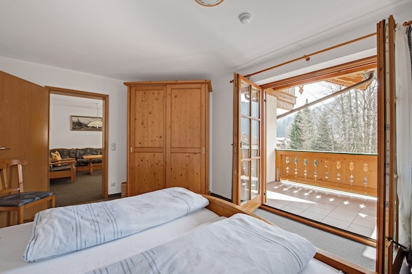 Une chambre avec deux lits, une armoire en bois et un balcon donnant sur la forêt.