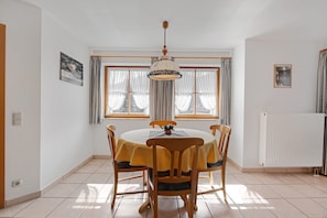 Un coin repas comprenant une table ronde, quatre chaises, un luminaire suspendu et une fenêtre avec des rideaux.