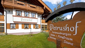 A wooden sign with 'Petrushof' and amenities listed, in front of a building with balconies and windows. - Apartment “Petrushof Ferienwohnung Taubensee” with Mountain View, Wi-Fi, Balcony (Oberwössen)