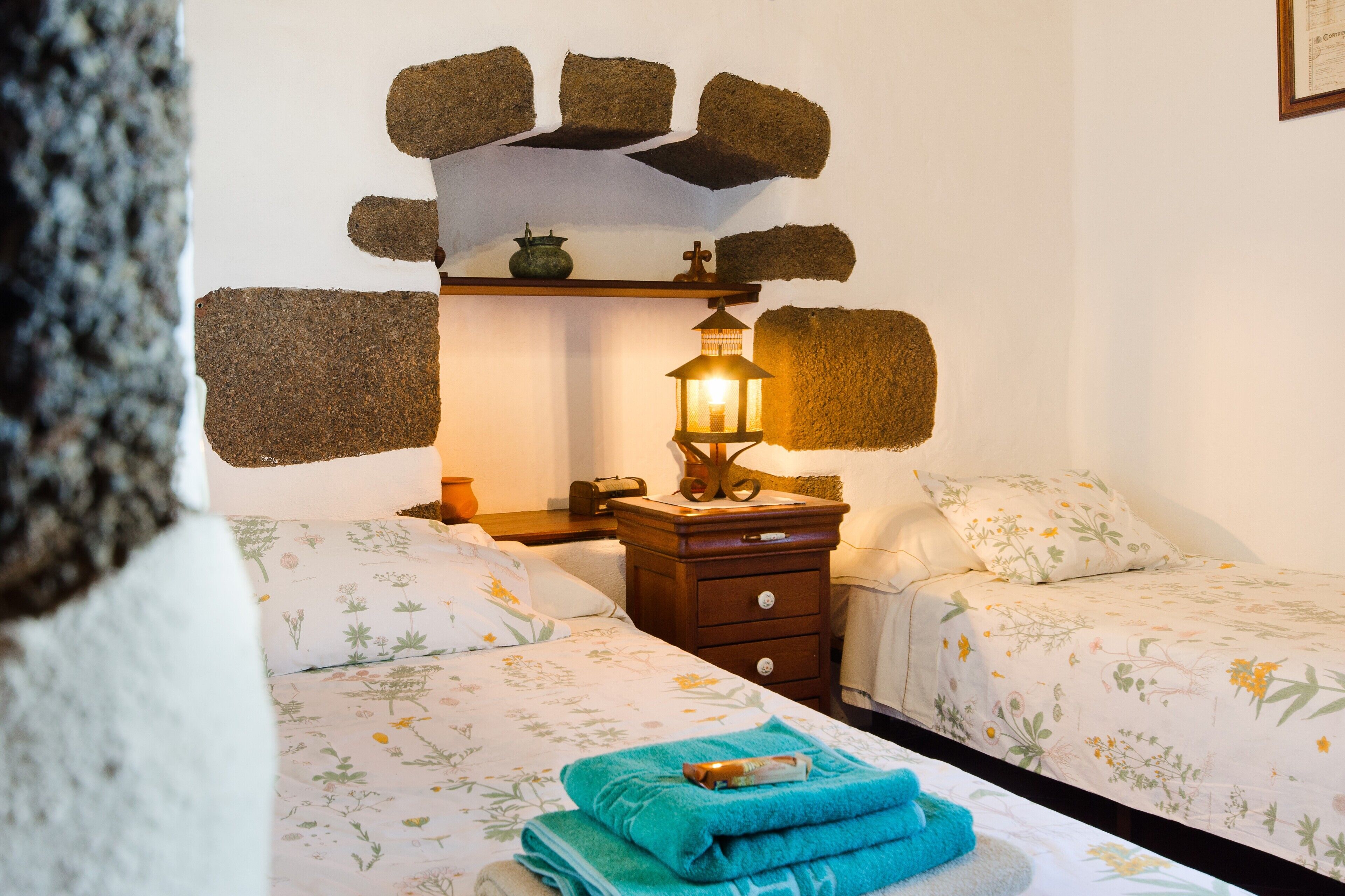 Une chambre avec deux lits, une table de chevet, une étagère murale agrémentée d’une lanterne, et un décor mural rustique.