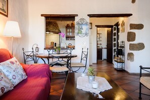 A cozy living room with a red sofa, a dining table with chairs, a kitchen in the background, and a stone wall.