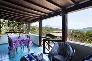 Un patio cubierto con una mesa y sillas, una silla con estampado de cebra, y vistas a montañas y follaje.