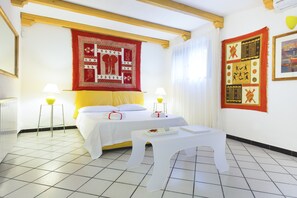 Una habitación de hotel con una cama, dos mesitas de noche, una pequeña mesa con una bandeja y dos lámparas de pared.