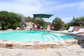 Una piscina con baldosas de piedra, sillas de descanso y sombrillas.