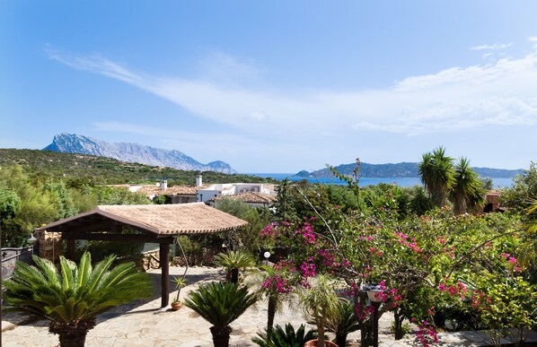 A patio with a pergola, potted plants, and a view of the sea and mountains.