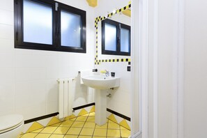 Un baño con un lavamanos blanco, un inodoro y una ventana con marcos negros.