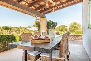 Une terrasse extérieure avec une table dressée pour le repas, des chaises en osier, un pilier en pierre et une vue sur le paysage environnant.