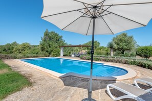 Une piscine agrémentée d’une pergola et de chaises longues, le tout entouré de verdure.