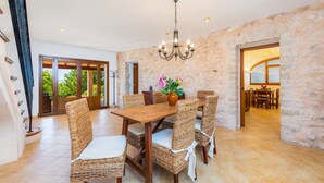 A dining area with a wooden table and wicker chairs, a chandelier, and a stone wall. - Holiday Home "Cas Batlet Antonia" with Pool, Terrace, Sea & Mountain View (S'HORTA)