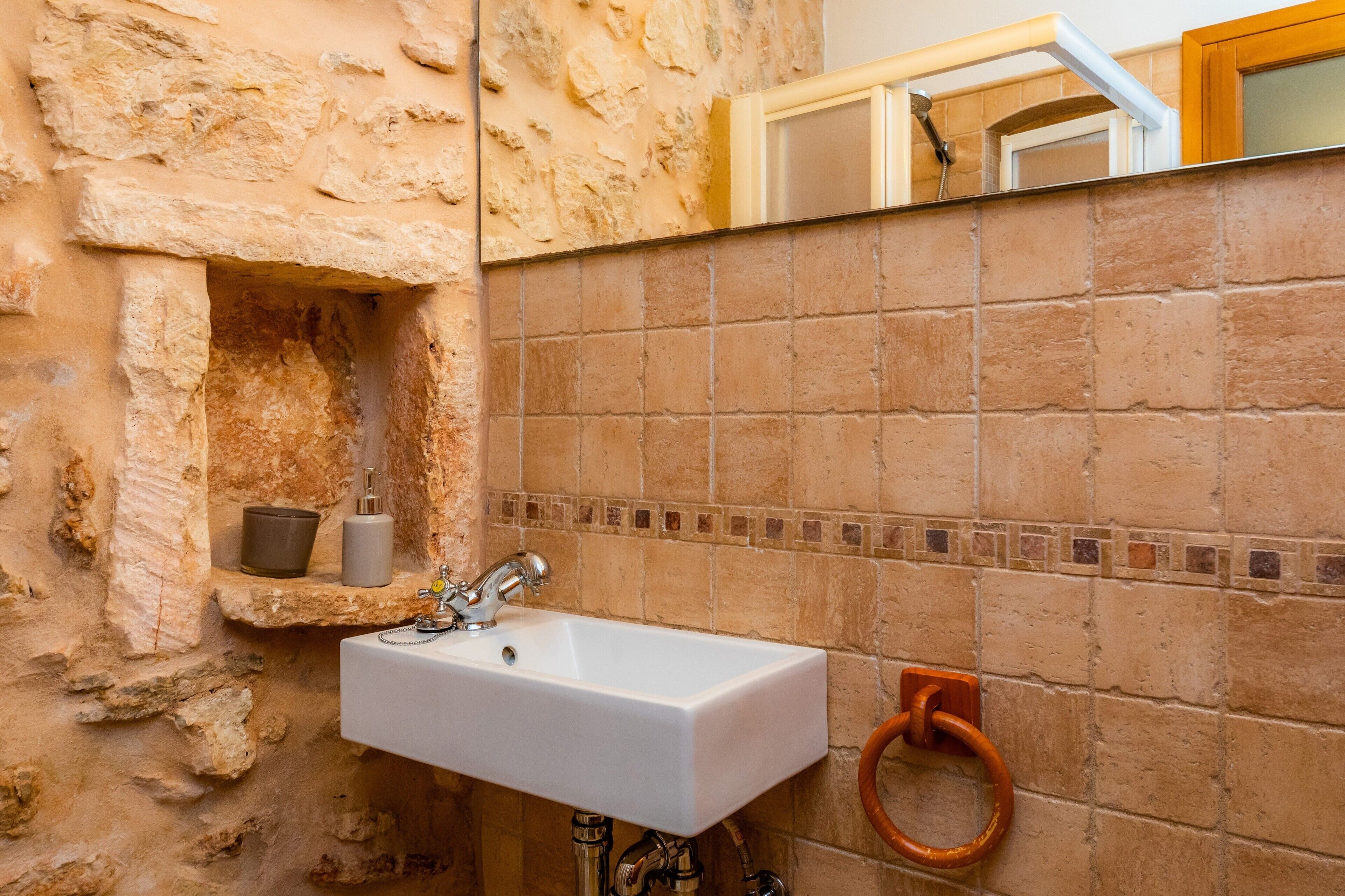 Un baño con pared de piedra, un lavamanos blanco, un espejo y un toallero.