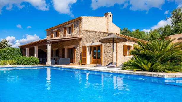 A stone villa with a swimming pool, a covered patio, and a view of the surrounding greenery. - Holiday Home "Cas Batlet Antonia" with Pool, Terrace, Sea & Mountain View (S'HORTA)