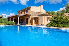 Una villa de piedra con piscina, un porche cubierto y vistas de la vegetación circundante.