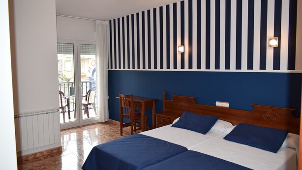 A hotel room with a large bed, a desk, and a chair. There is a window with a view of the outside.